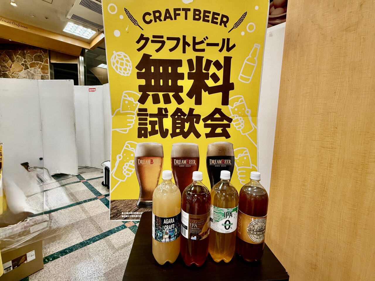 「クラフトビール無料試飲会」のポスターとビールボトルが並ぶ会場入口